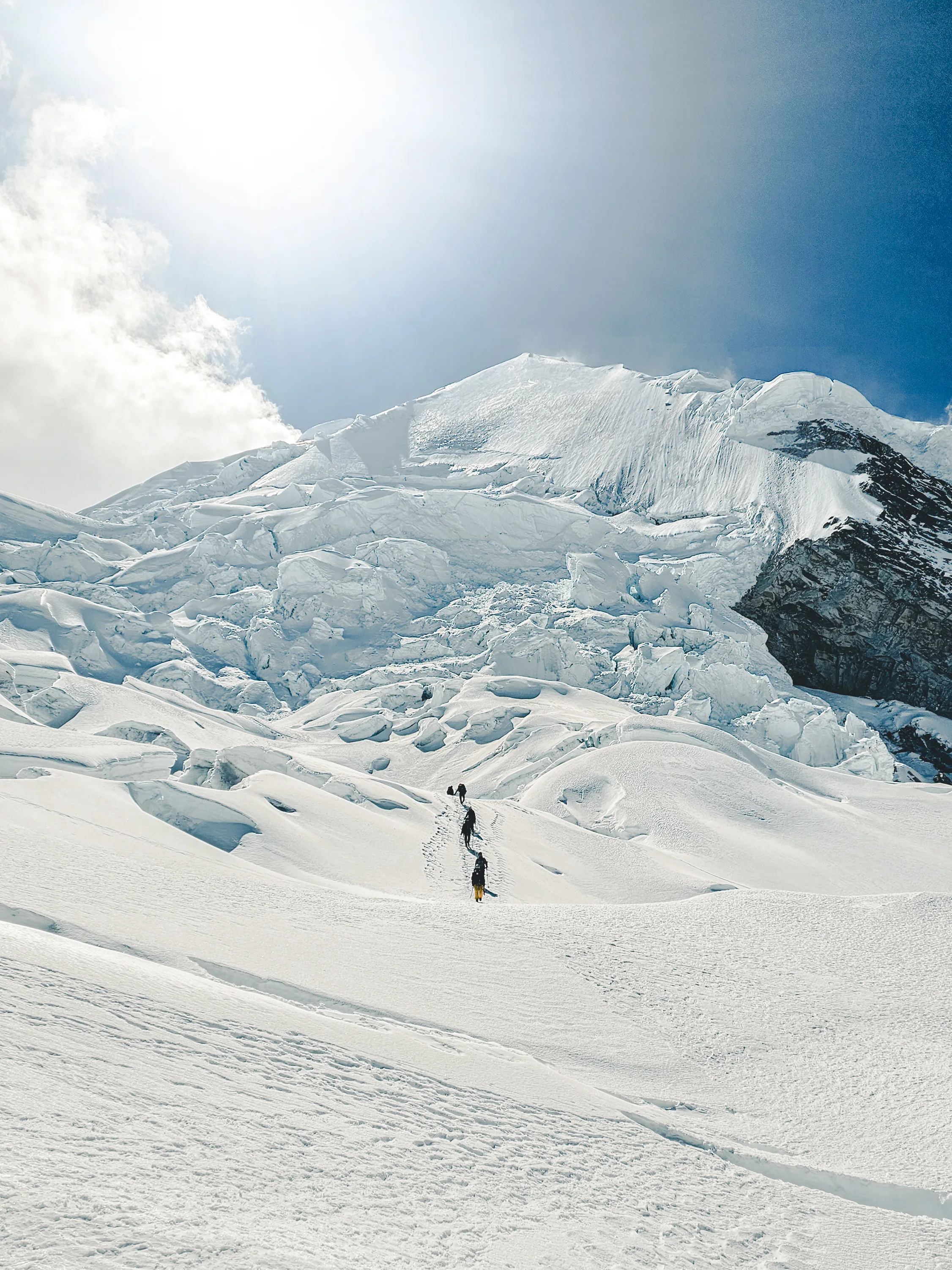Vertical view of a huge glacier and icefall on Nevado Huascarán under a bright sun, climbers tiny on the snow far below, Cordillera Blanca, Peru