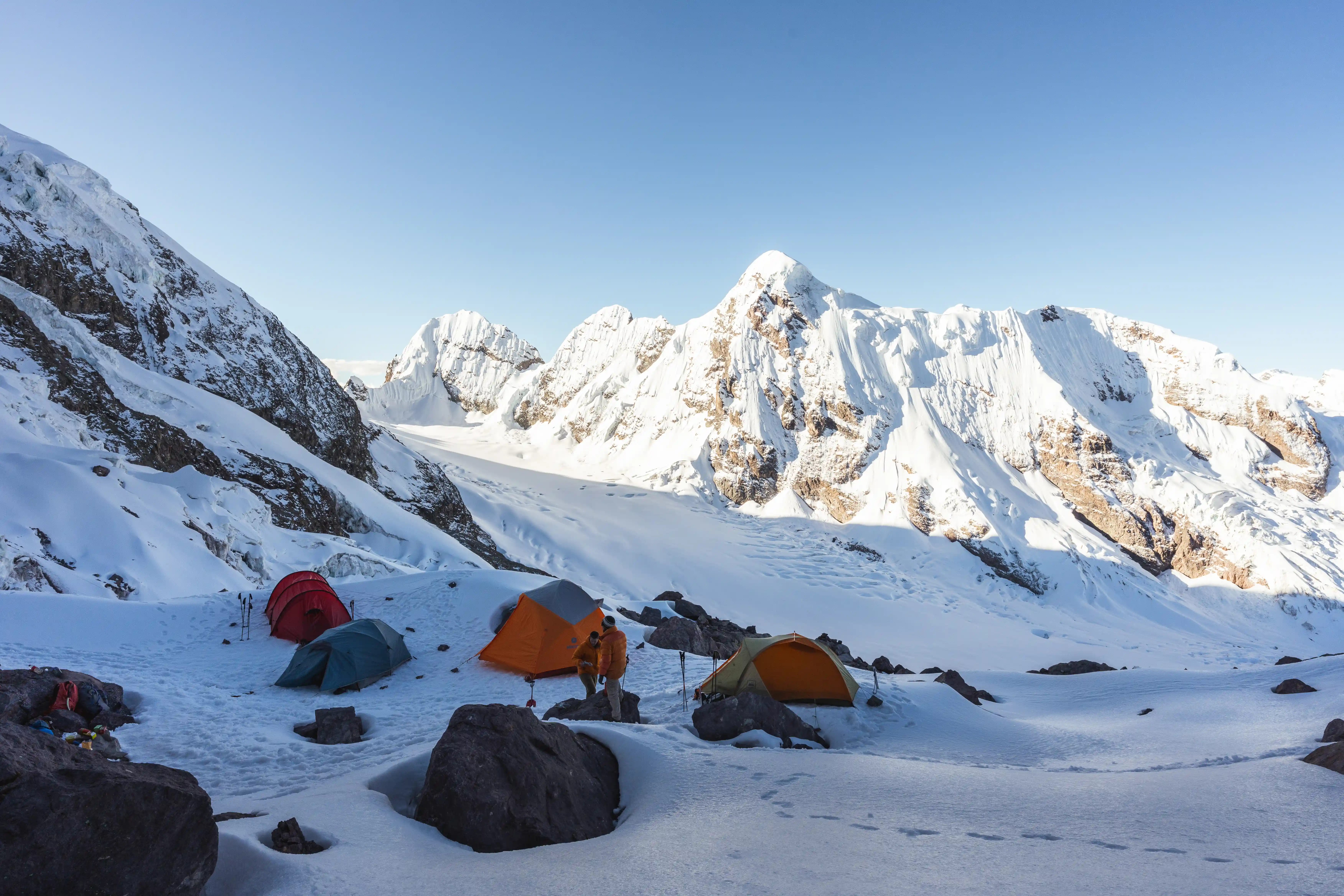 Several tents pitched on snow-covered moraine in morning light, a wall of glaciated peaks rising behind the camp, Nevado Ausangate, Peru