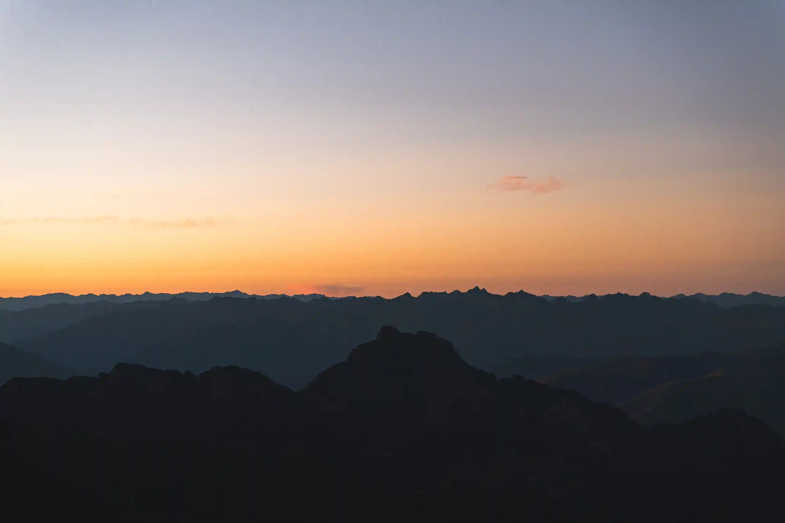 Layer upon layer of dark ridges fading towards the Amazon basin under an orange dawn sky, from Nevado Sirijuani base camp, Peru